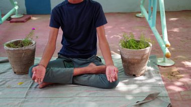 Bir çocuk Hindistan 'da evinde meditasyon yapıyor. Nilüfer pozisyonunda oturan geleneksel siyah gömlekli Hintli genç çocuk..