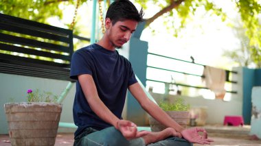 Bir çocuk Hindistan 'da evinde meditasyon yapıyor. Nilüfer pozisyonunda oturan geleneksel siyah gömlekli Hintli genç çocuk..