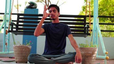 Bir çocuk Hindistan 'da evinde meditasyon yapıyor. Geleneksel siyah tişörtlü Hintli çocuk yoga pozisyonunda oturuyor..