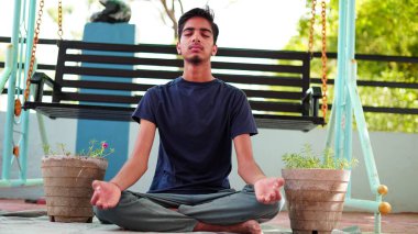 Bir çocuk Hindistan 'da evinde meditasyon yapıyor. Geleneksel siyah tişörtlü Hintli çocuk yoga pozisyonunda oturuyor..