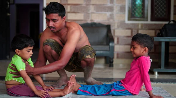 Portrait of trainer helping while kids are practising yoga by bending backwards on mats at home.