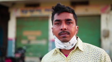 Maskeli bir adam kapalı pazar arka planında dikilirken kameraya bakıyor.