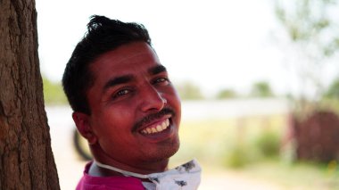 Sert bir geçmişi olan gülümseyen Hintli genç adamın portresi. Mutlu Asyalı adam dışarıda kameraya bakıyor..