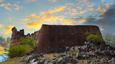 Eski bir duvar ve dağılan kalıntılar gün batımında bir kalenin parçalarıdır. Gökyüzü arka planında dramatik bulutlar olan antik bir kalenin dış duvarı..