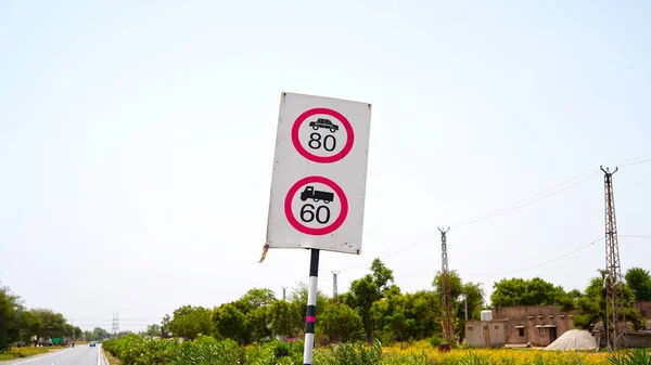 Limit Speed Sign Board of running vehicles with 80 and 60 speed. Vehicles passing through road against blue sky background.