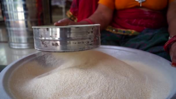 Erwachsene indische Frau sieben Mehl Weizen aus einem Sieb, um Essen zu kochen. Indisches Lebenskonzept auf dem Land. — Stockvideo