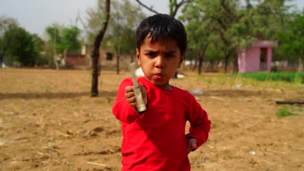 Röd T-shirt pojke som håller en väderkvarn i handen och spelar på fältet. Begreppet barndom. — Stockvideo