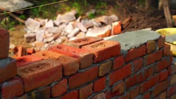 Gamle indiske byggarens hand sätter tegelstenen i muren. Närbild stängning av Bricklayer arbetar på en grön fält bakgrund — Stockvideo