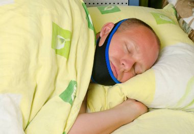 Yetişkin bir adam horlayan bir bandajla yatakta uyuyor. 