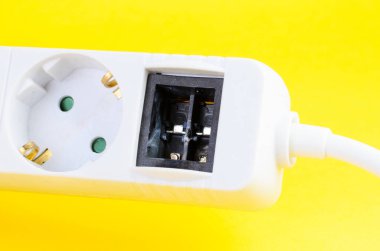 Eksik aşırı yükleme koruma düğmesini gösteren üç prizli beyaz güç şeridine yakın plan, elektriksel tehlike, ev veya ofis ekipmanları ve güvenlik endişelerini gösteren.