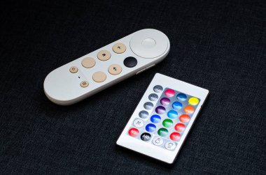 İki uzaktan kumanda karanlık bir yüzeye oturur, biri akıllı bir televizyon için, diğeri LED ışıkları kontrol etmek için.