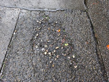 Hasarlı asfalt yüzeyinde çatlaklar ve pürüzlü dokular var. Küçük çukurlar ve ıslak alanlar görünüyor. Tasarım, doku ve yüzey kavramları için mükemmel şehir arkaplanı.