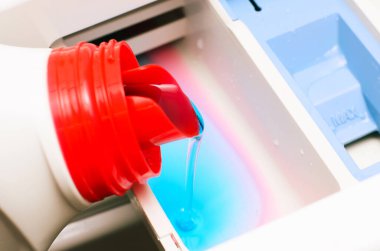 Yakın çekim çamaşır makinesinin makinesine çamaşır deterjanı dökme sürecini gösteriyor.