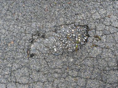 Çatlak asfaltta aşınma ve yırtık izleri var. Çukur, çakıl ve küçük taşlarla dolu.