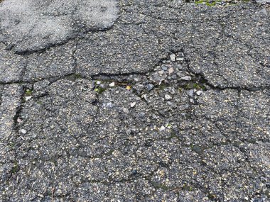 Bu resim hasarlı asfalt yüzeyin yakın çekimini gösteriyor, çatlakları ve açıkta kalan toplam