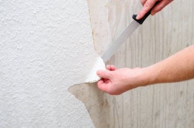 Bir kişi, ev geliştirme projesi sırasında eski duvar kağıtlarını dikkatlice soymak için bıçak kullanıyor.