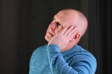 Yüzünde eli olan bir adam düşünceli bir ifadeyle yukarı bakıyor.