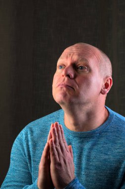 Elleri duada sıkıca bağlanmış bir adam, dalgın bir ifadeyle yukarıya bakıyor.