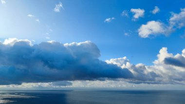 Okyanusun uçsuz bucaksız genişliği çarpıcı bulutların ve mavi gökyüzünün altında uzanır.