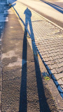 Öğleden sonra güneşinde kaldırımda bir insanın uzun gölgesi.