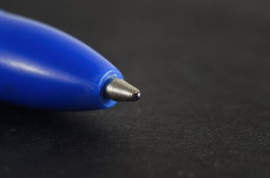 Koyu dokulu bir yüzeyde mavi tükenmez kalem ucunun aşırı yakın plan makro çekimi.