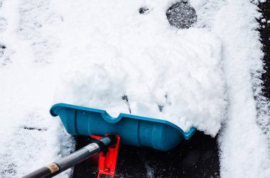 Mavi plastik kürek, asfaltlı yüzeyden taze beyaz kar kaldırıyor..