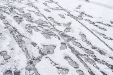 Dağınık ayak izleri ve lastik izleri asfalt bir sokakta taze beyaz kar içinde..