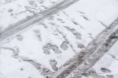 Urban winter footprints and tire tracks on snowy slushy asphalt road