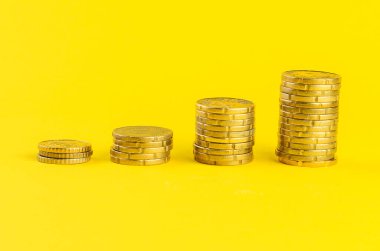 Yığınla altın madeni para, parlak sarı arkaplana karşı yükseliyor.