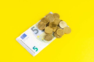 Beş avroluk banknota, parlak sarı bir fona saçılmış avro sikkeleri