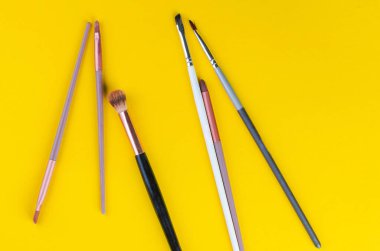 Güzellik içeriği için canlı sarı arkaplanda çeşitli makyaj fırçaları düzenlendi