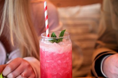 Refreshing pink cocktail with mint and ice, served in a glass with a striped straw