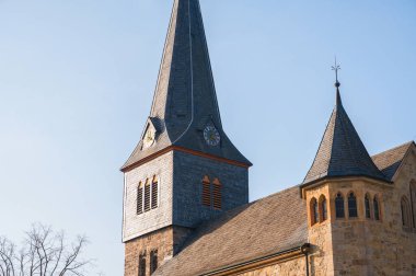 ISERLOHN, GERMANY - 27 Mart 2026: Açık mavi gökyüzüne karşı Letmathe 'deki tarihi St. Kilian Kilisesi' nin (Kilianskirche) tahta kaplamalı kilise kulesinin ve çan kulesinin yakın çekimi.