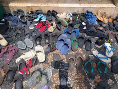 Denpasar, Bali, Endonezya. 13 Aralık 2025. Bali 'de bir caminin girişinde sandalet ve ayakkabı yığınları..