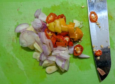 Ingredients such as chopped shallots, garlic, and chilies are prepared on a green chopping board for a spicy culinary creation.