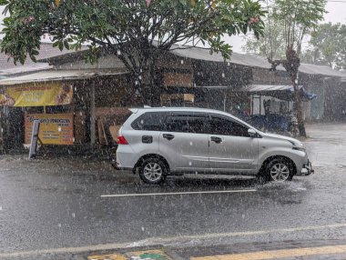 Denpasar, Bali. 19 Aralık 2025. Gümüş renkli bir araba Denpasar şehir yolunda şiddetli yağmura göğüs gerdi.