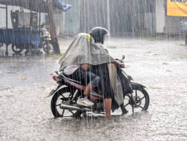 İki motosikletli yağmurlu havada su birikintilerinde yağmurluk giyiyor..