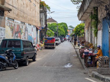 Denpasar şehrinde sabah atmosferinde sokak satıcıları, park etmiş araçlar ve duvarlarla süslenmiş duvarlar var.