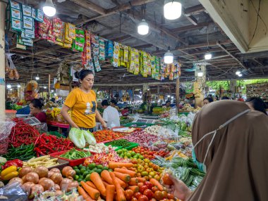 İnsanlar çeşitli meyve ve sebzelerin sergilendiği hareketli bir açık hava pazarından alışveriş yapıyorlar..