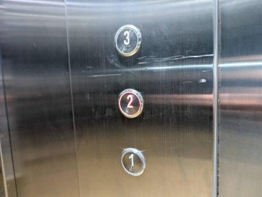 Asansör kontrol düğmeleri yansıtıcı metal panelde daireseldir..