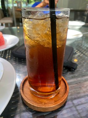 Eriyen buzla dolu ferahlatıcı bir bardak buzlu çayın yakın çekimi ve şık bir ahşap bardak altlığında yoğunlaşma. Bir kafede mükemmel bir yaz içkisi..