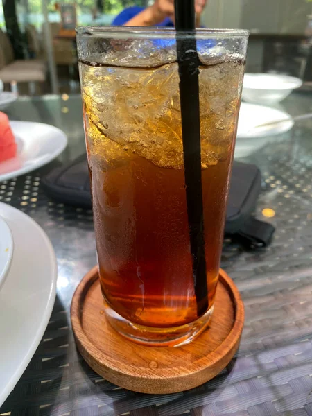 Eriyen buzla dolu ferahlatıcı bir bardak buzlu çayın yakın çekimi ve şık bir ahşap bardak altlığında yoğunlaşma. Bir kafede mükemmel bir yaz içkisi..