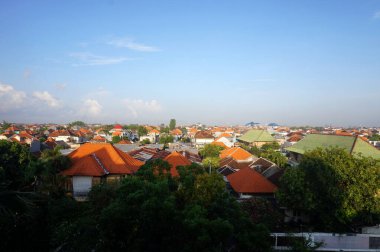 Kırmızı ve yeşil kiremit çatılı yoğun yerleşim yerlerinin panoramik hava manzarası parlak mavi gökyüzü altında yemyeşil tropikal ağaçlarla kesişiyor. Kentsel yayılma.