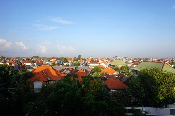 Kırmızı ve yeşil kiremit çatılı yoğun yerleşim yerlerinin panoramik hava manzarası parlak mavi gökyüzü altında yemyeşil tropikal ağaçlarla kesişiyor. Kentsel yayılma.