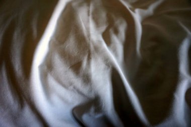 Pürüzsüz beyaz kumaşın yakın çekim soyut dokusu ya da derin kırışıklıklar ve dramatik gölgeler gösteren yatak örtüsü. Minimalist tekstil arka planı ya da yüzey olarak ideal.