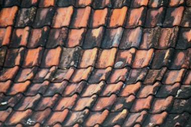 Eski yıpranmış terracotta çatı fayanslarının soyut görüntüsü dokulu bir arka plan oluşturuyor. Yüzeyde siyah yosun ve turuncu yaşlanma lekeleri var..