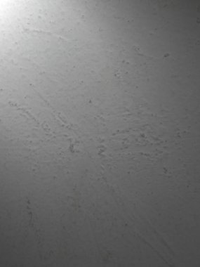 Hafif lekeler ve pürüzlü pürüzlü yüzey içeren sıkıntılı, açık gri duvar dokusuna yakın çekim. Sol üst spot ışığı tarafından aydınlatılarak karanlık bir eğilim yaratıldı..