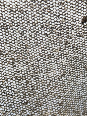 Eski, kirli, altıgen tel örgülü bir ekranın makro görüntüsü. Arkaplanda birikmiş enkaz ve kirle dolu ayrıntılı bal peteği deseni deseni.