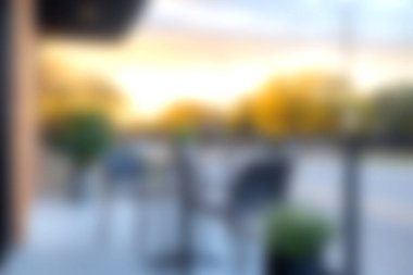 Gün batımında bulanık sandalyeler ve masaların olduğu güzel bir açık kafe. Ilık parıltı rahatlamak için davetkar atmosferi güçlendirir..