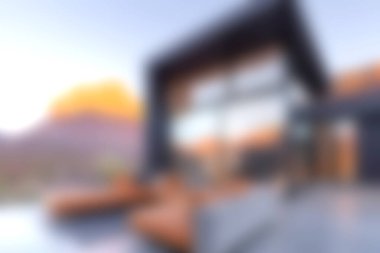 Bu resim, büyük cam pencereli modern lüks bir ev sunuyor, günbatımında doğanın çarpıcı manzarasını sergiliyor, zarafet ve konforu birleştiriyor..